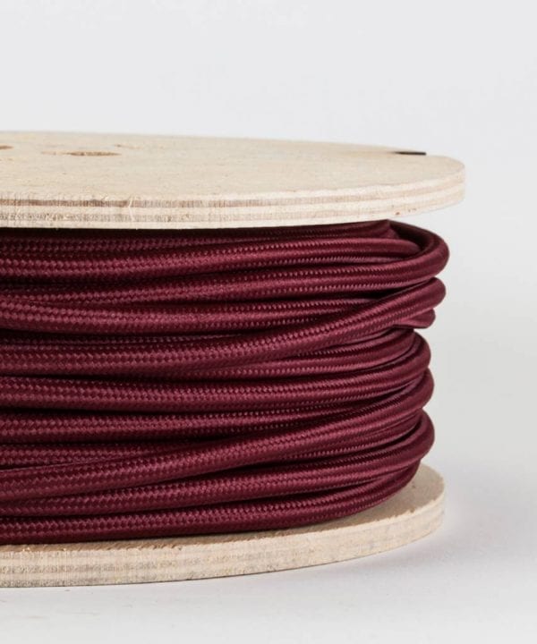 closeup of burgundy fabric cable on reel against white background