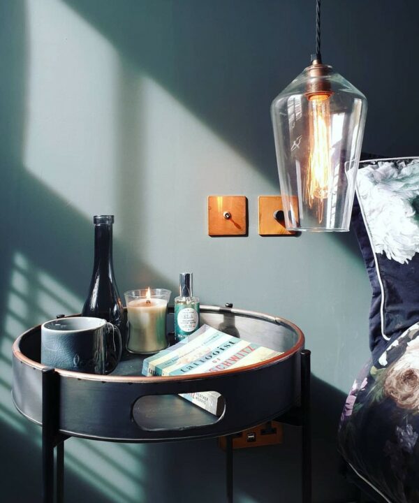 copper and black single togle and single dimmer installed on a dark blue wall above a bedside table