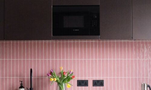 black double socets installed on a pink tiled wall in a black and pink kitchen