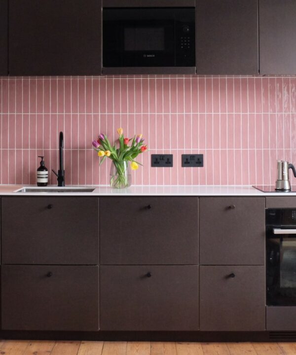 black double socets installed on a pink tiled wall in a black and pink kitchen