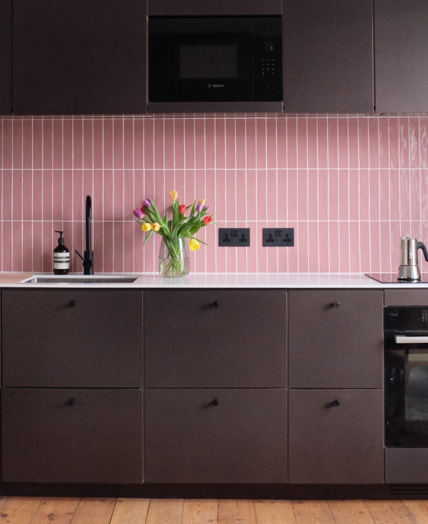 black double socets installed on a pink tiled wall in a black and pink kitchen