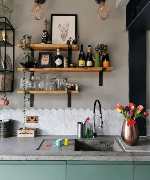 tarnished copper and black double socket on an off-white geometric tiled wall in a grey and green kitchen