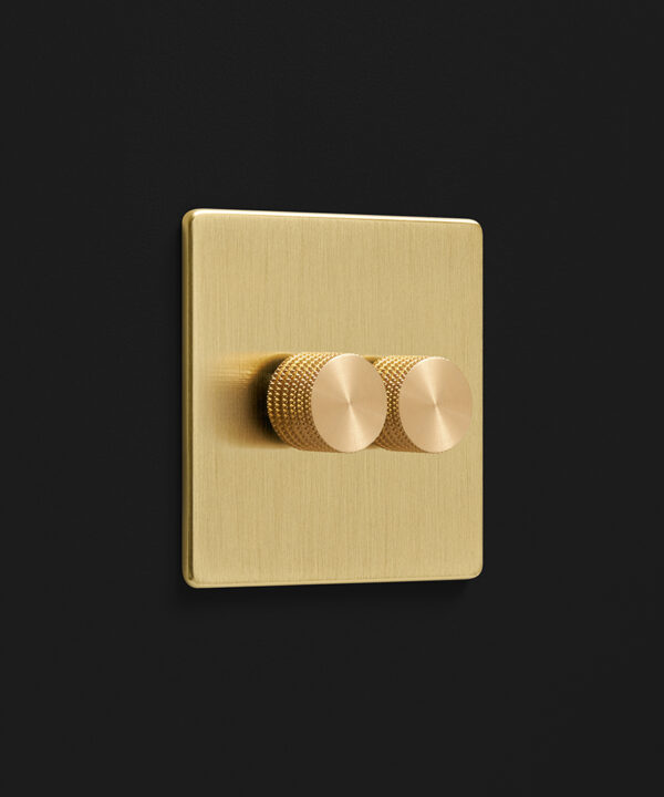 brushed gold double dimmer light switch with two knurled gold dimmer knobs photographed on a black background