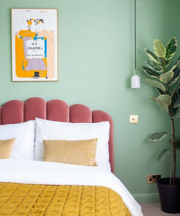 gold single dimmer switch installed on a mint green wall beside a pink velvet scalloped headboard in a bedroom