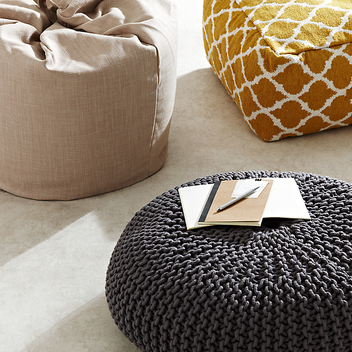 grey chunky knitted footstool, yellow patterned stool and beige beanbag on neutral carpet