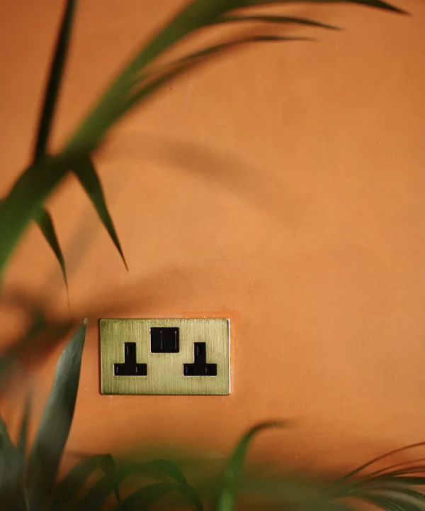 Gold double plug socket against an orange wall.