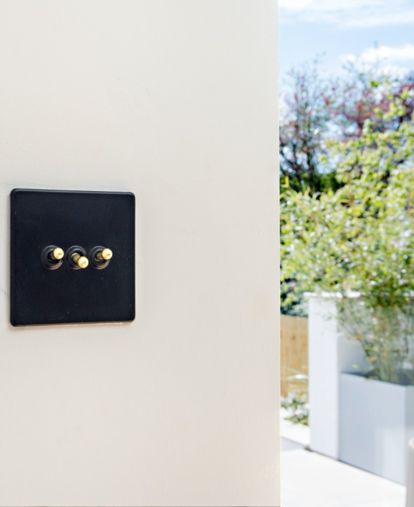 black and gold triple toggle on an off-white wall beside a window