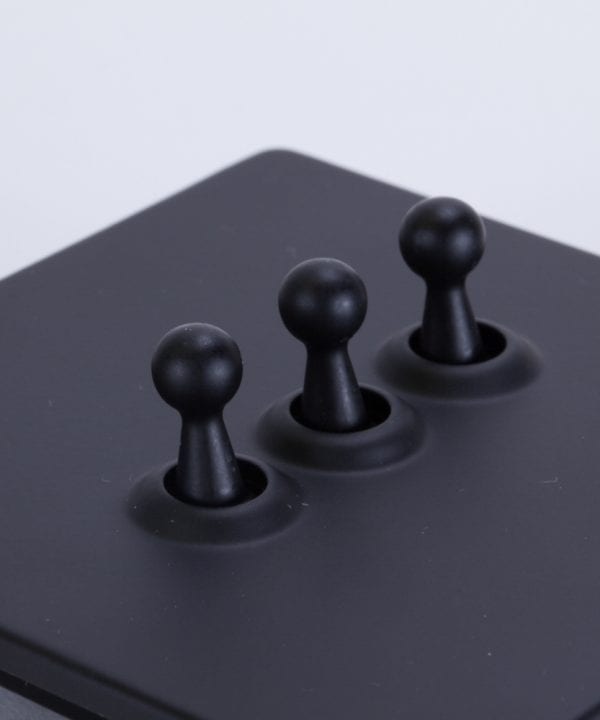 closeup of black and black triple toggle switch against white background