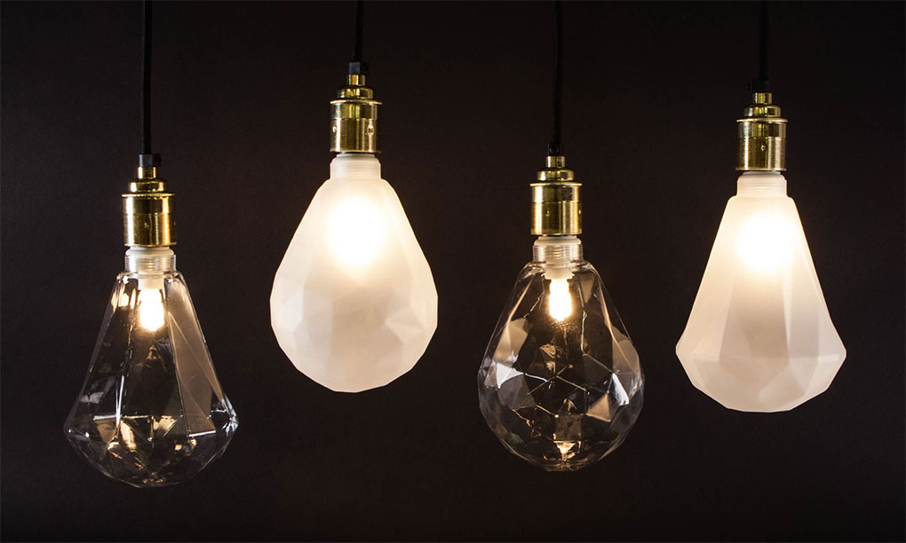 geometric light bulbs suspended from gold bulb holders against black background