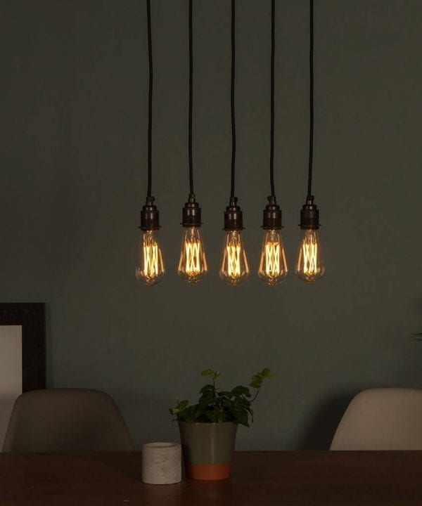 Large pear squirrel cage filament LED warm light bulbs suspended in a series above a table on dark grey background