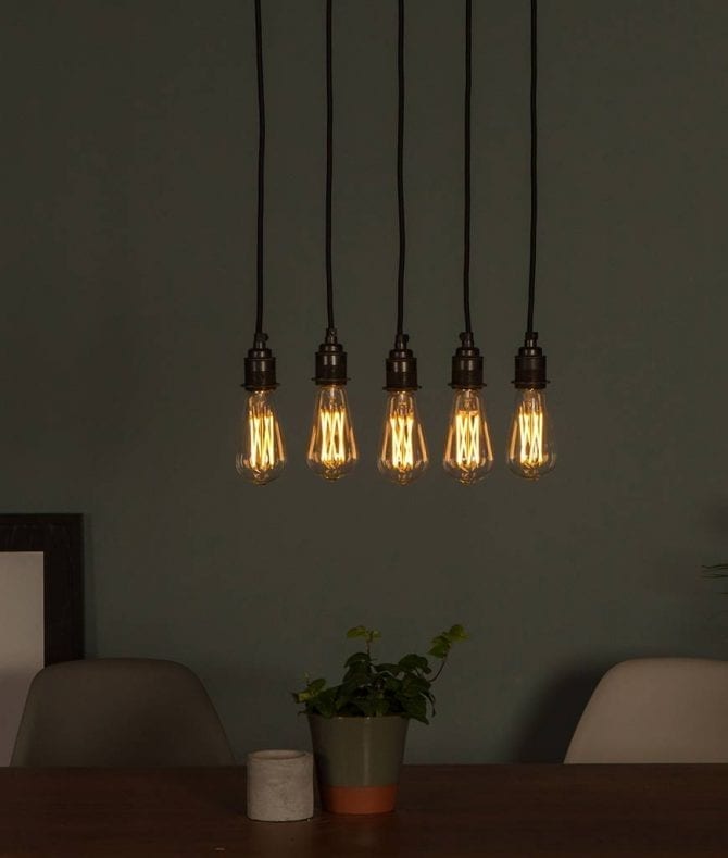 Large pear squirrel cage filament LED warm light bulbs suspended in a series above a table on dark grey background