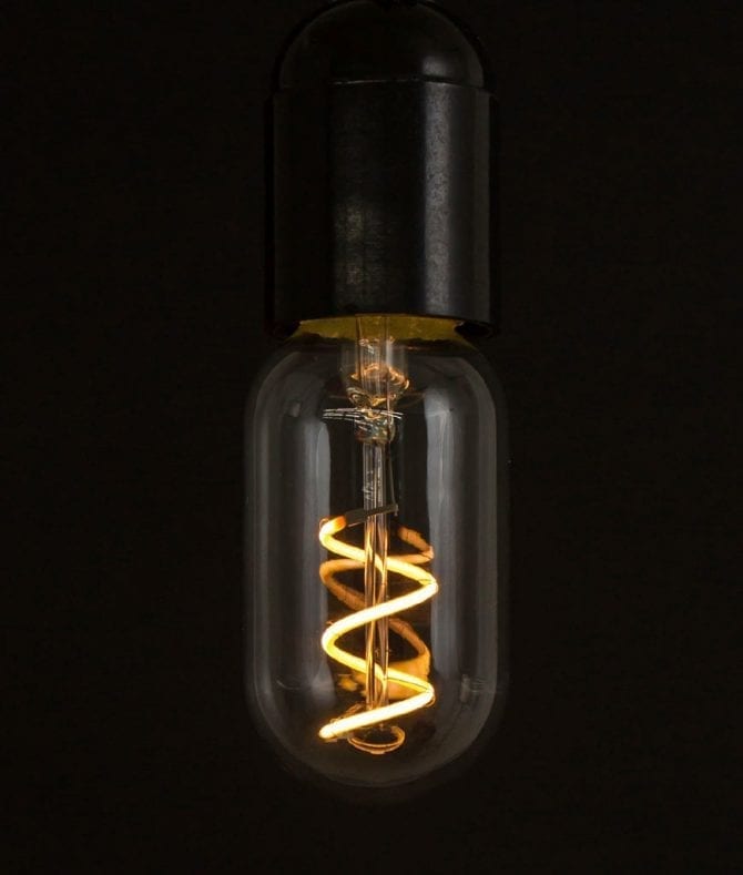 radio valve led filament bulb with loose spiral filament lit suspended from bakelite bulb holder against black wall