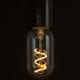 radio valve led filament bulb with loose spiral filament lit suspended from bakelite bulb holder against black wall