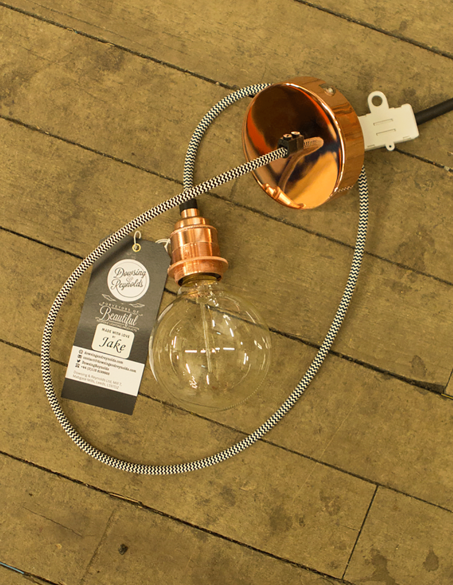 ceiling pendant made uip using copper ceiling rose, black and white fabric cable, copper bulb holder and quad loop bulb laying on a wooden floor