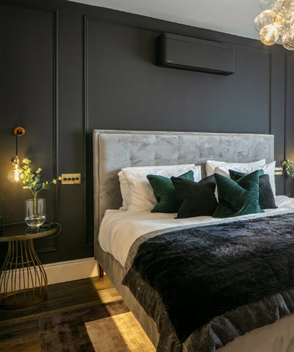 smoked gold and black quadruple dimmer installed on a black panelled wall beside a grey velvet headboard.