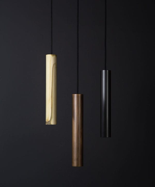 baton tube pendant light, three steel tube spotlights in smoked gold, antique and black, suspended from black fabric cable against a black wall