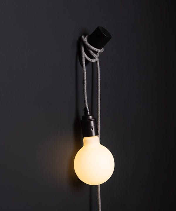 black peg lamp with grey jumper cable against black wall