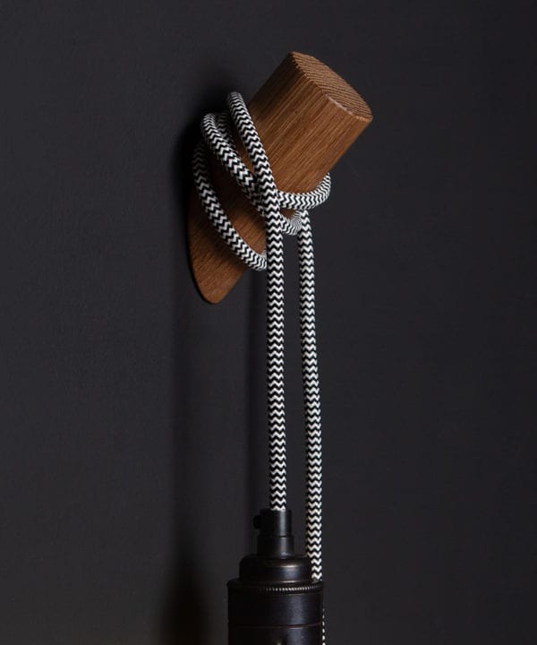 closeup of peg wall light danish oil with mint humbug cable on black wall