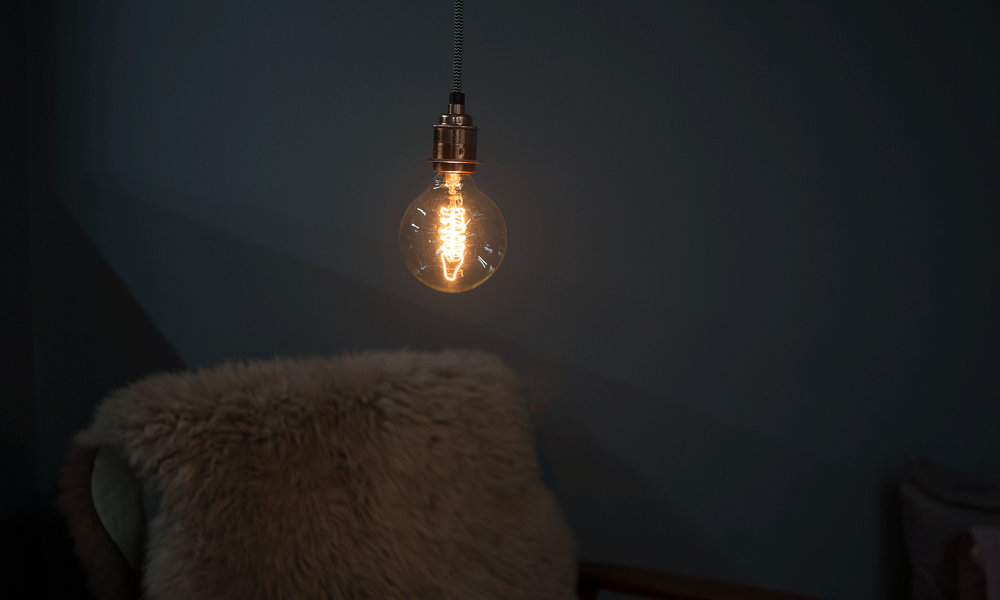 globe spiral filament bulb with silver bulb holder and black and white fabric cable against black background