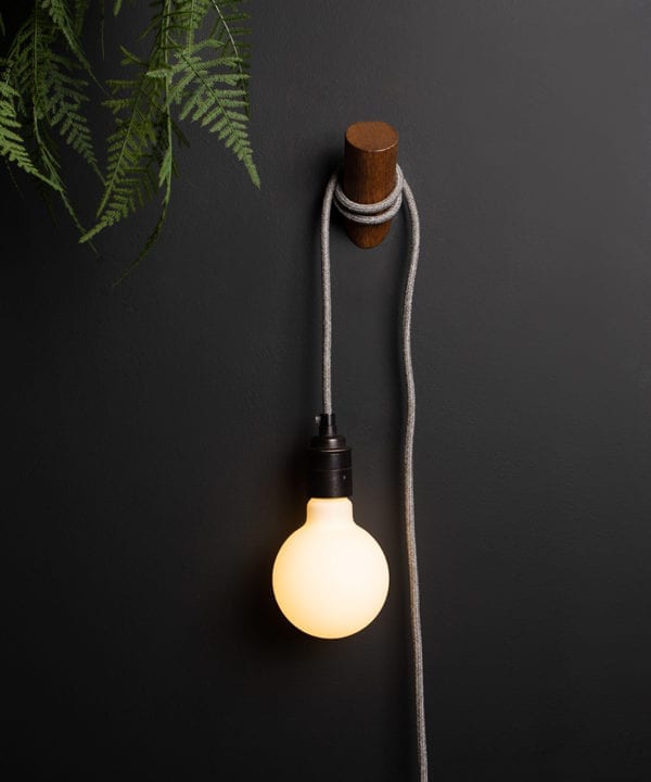 peg plug in wall lamp with dark oak peg and grey fabric cable against black wall