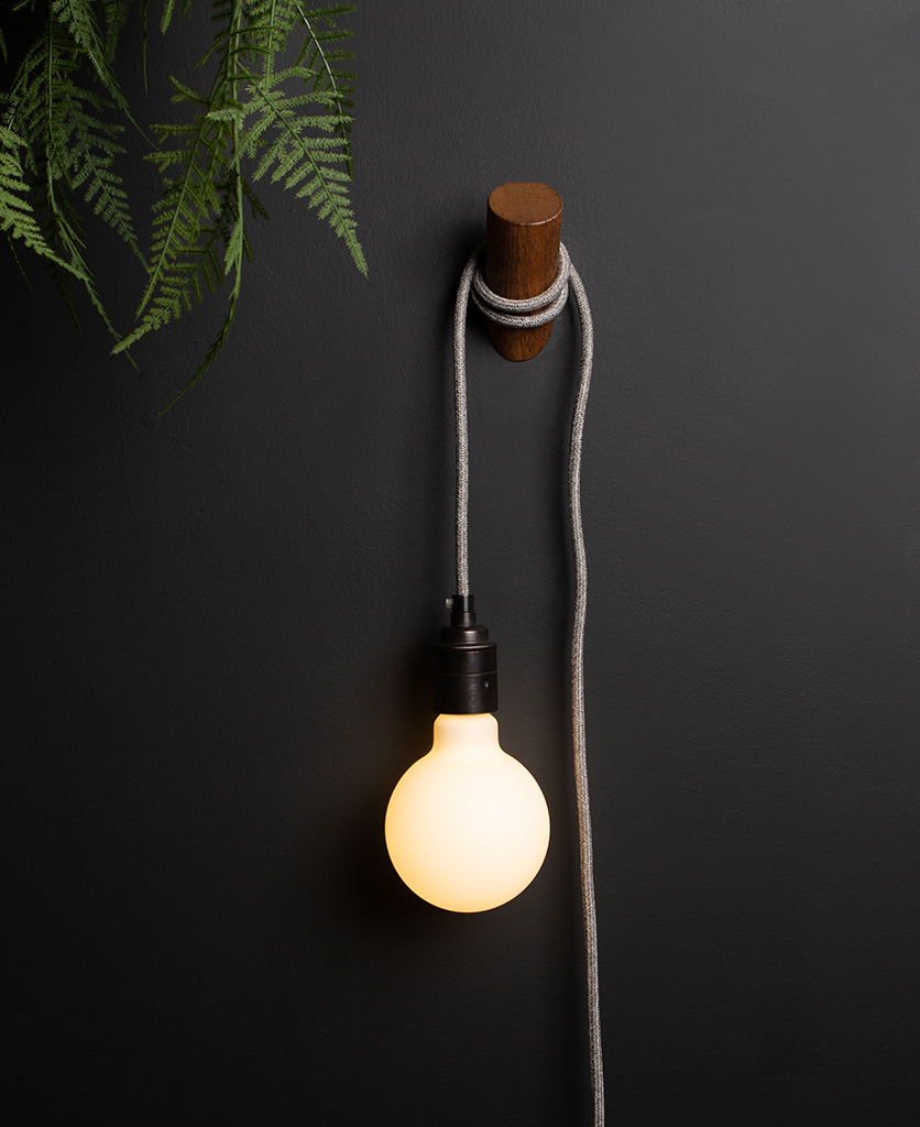 peg plug in wall lamp with dark oak peg and grey fabric cable against black wall