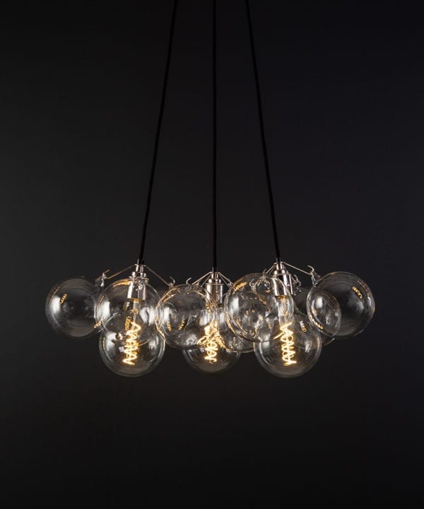 bubble pendant chandelier with 12 clear glass baubles and 3 silver bulb holders suspended from black fabric cable against a black wall