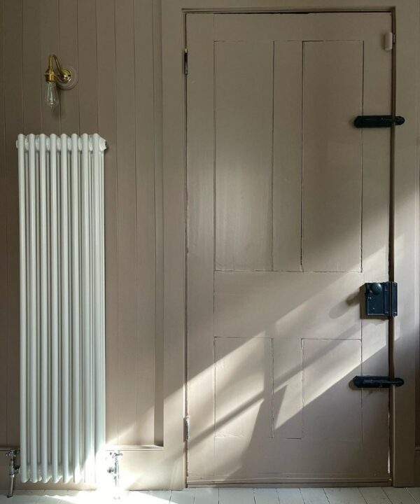 gold bramley wall light installed above a white radiator on a neutral wood panelled wall