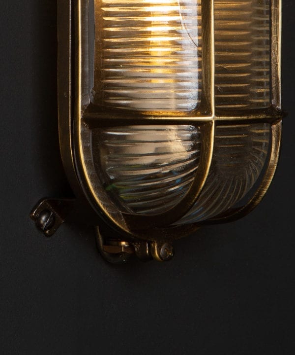 closeup of lit dave aged brass bulkhead light against black background