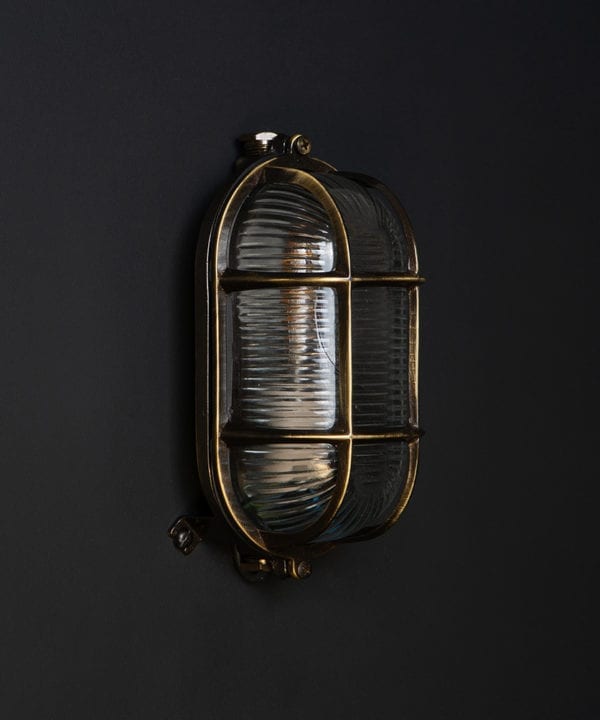 unlit dave aged brass outdoor bulkhead light against black background