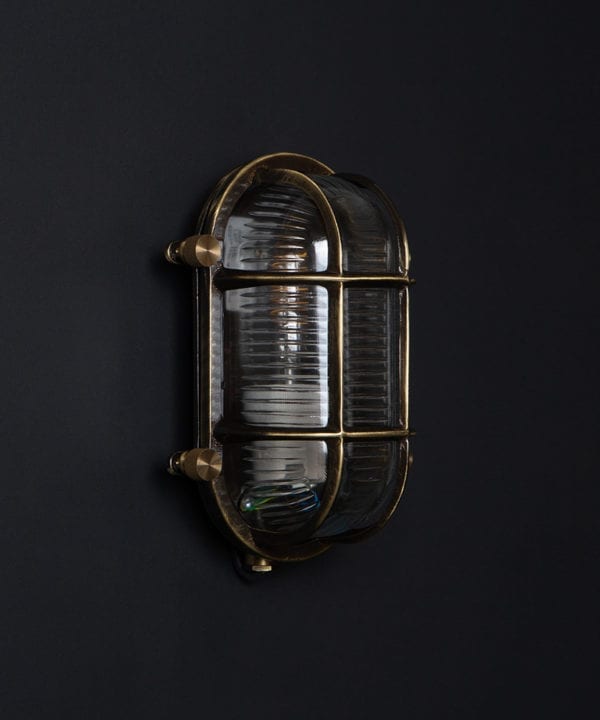 steve unlit aged brass bulbkhead light with posh knobs against black background