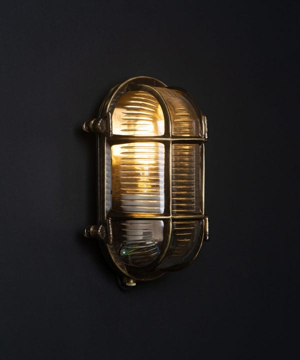 steve aged brass bulkhead outdoor lights with lit bulb against black background