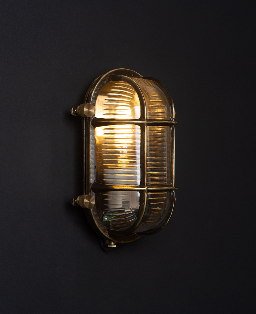 steve lit aged brass bulbkhead light with posh knobs against black background