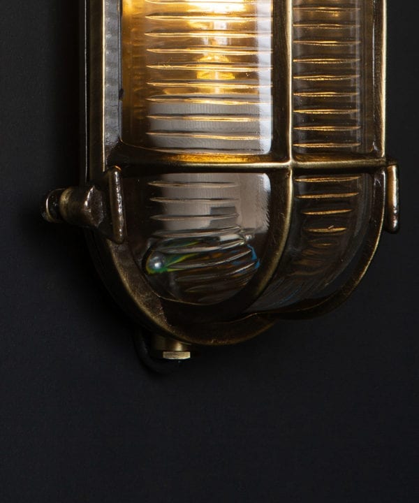 closeup of steve aged brass bulkhead outdoor lights with lit bulb against black background