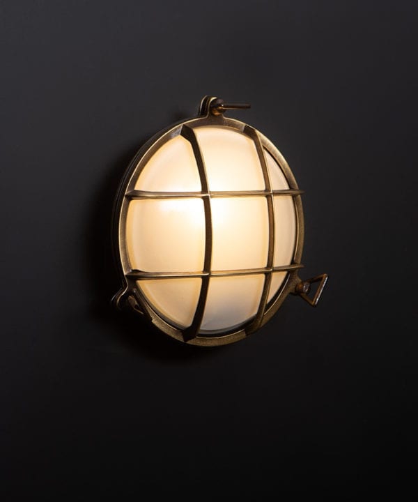 chris aged brass Bulkhead LED light with lit bulb on black wall