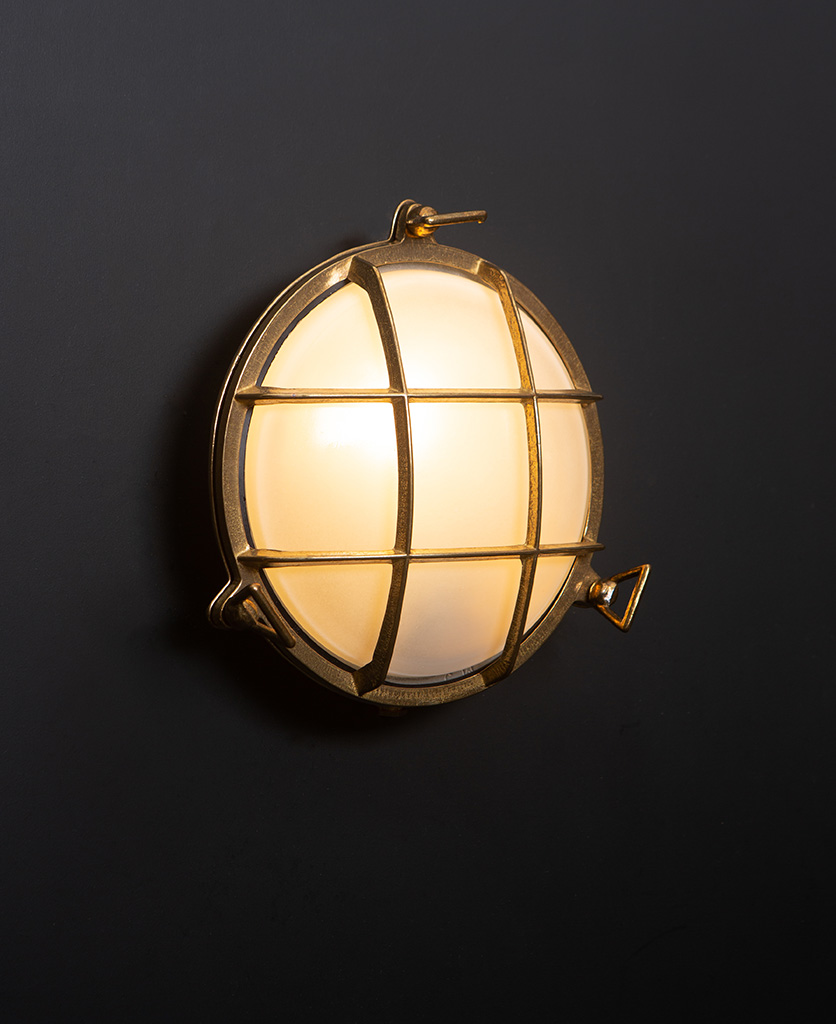 chris brass Bulkhead LED Light with lit bulb on black wall