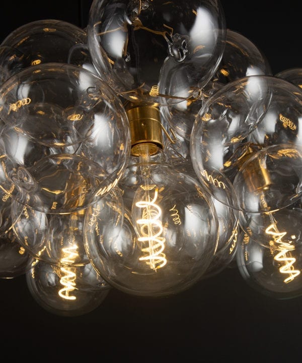 closeup of gold bubble glass chandelier with gold bulb holders and spiral filament light bulb against a black wall