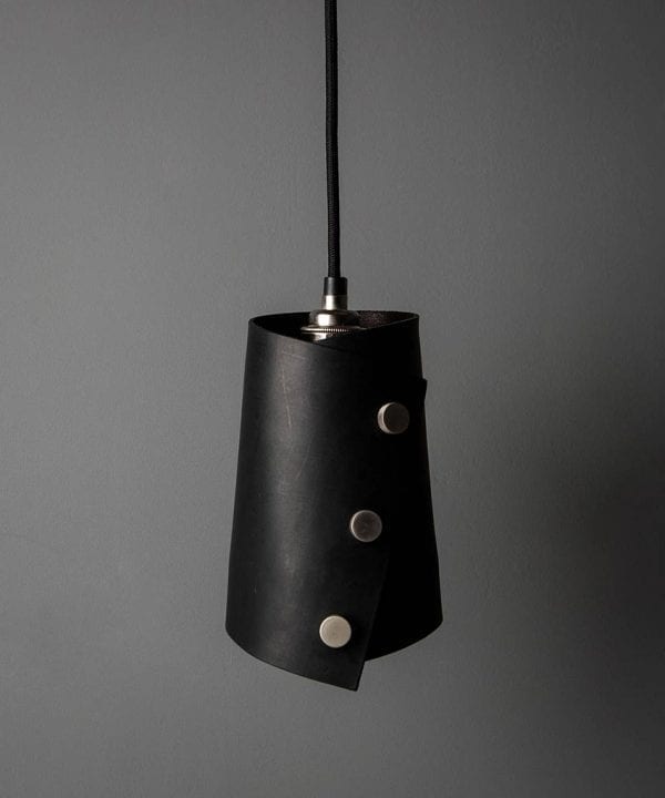 leather finish cuff pendant with black leather shade secured with knurled silver knobs, black fabric cable against dark grey background