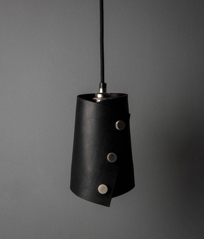 leather finish cuff pendant with black leather shade secured with knurled silver knobs, black fabric cable against dark grey background