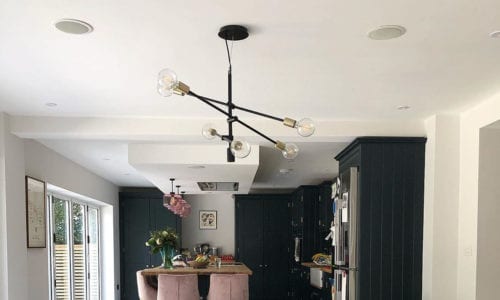 Trikonasana black multi-arm light suspended over a wooden dining table in a black and white kitchen