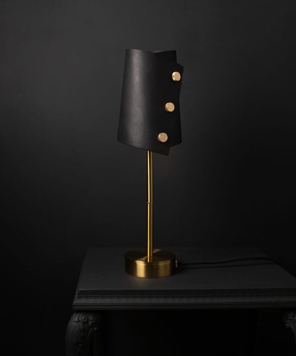 Leather desk lamp with black leather shade and brass base against black background