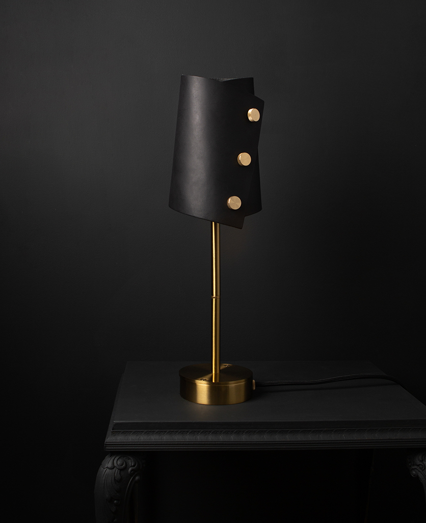 Leather desk lamp with black leather shade and brass base against black background