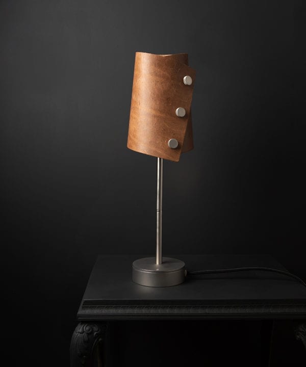 Leather lamp with tan leather shade and silver base against black background