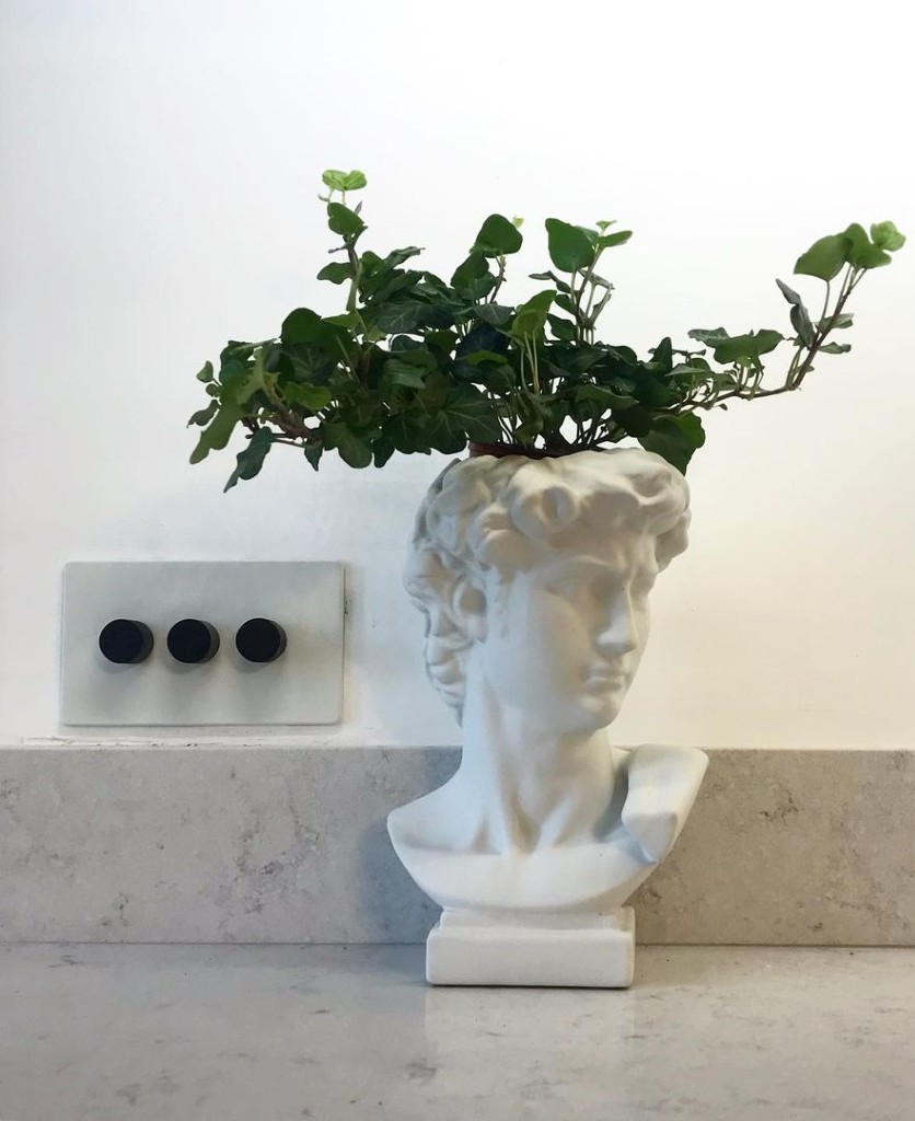 white and black triple dimmer installed on a white wall besides a white Grecian bust plant pot