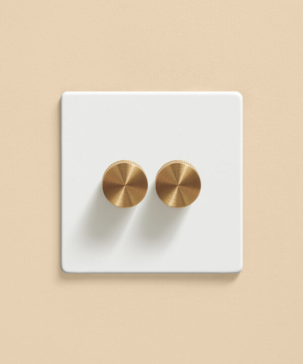white doubel dimmer switch with gold knurled knobs on a warm apricot wall