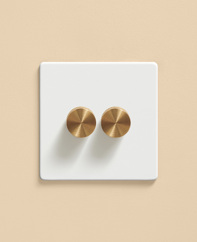 white doubel dimmer switch with gold knurled knobs on a warm apricot wall