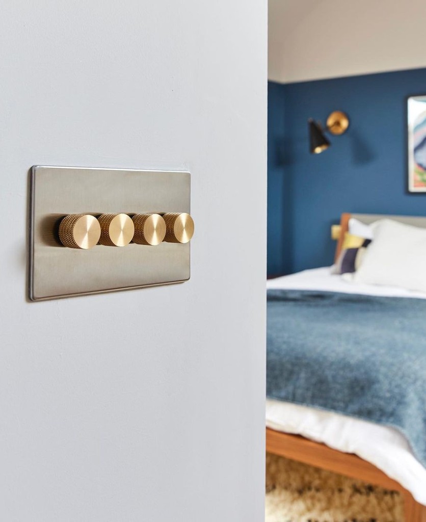 silver and gold quadruple dimmer switch installed on an off white wall in a navy and grey bedroom