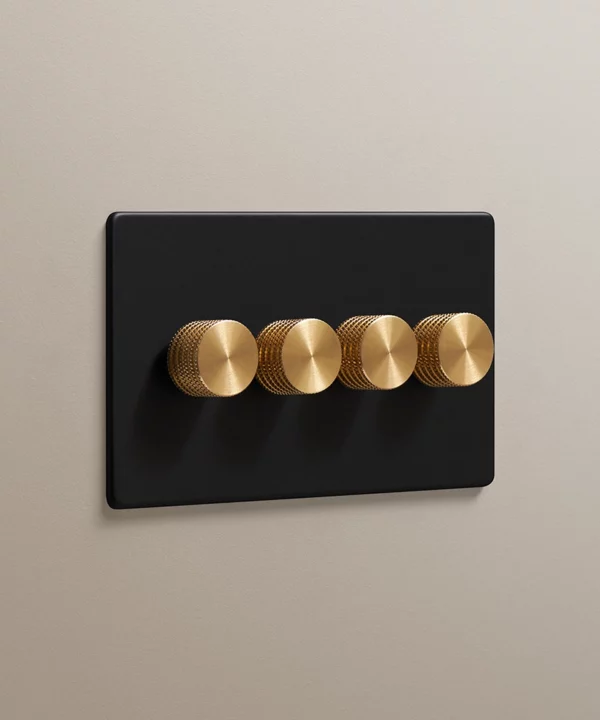black quadruple dimmer switch with gold knurled knobs on a stone coloured wall