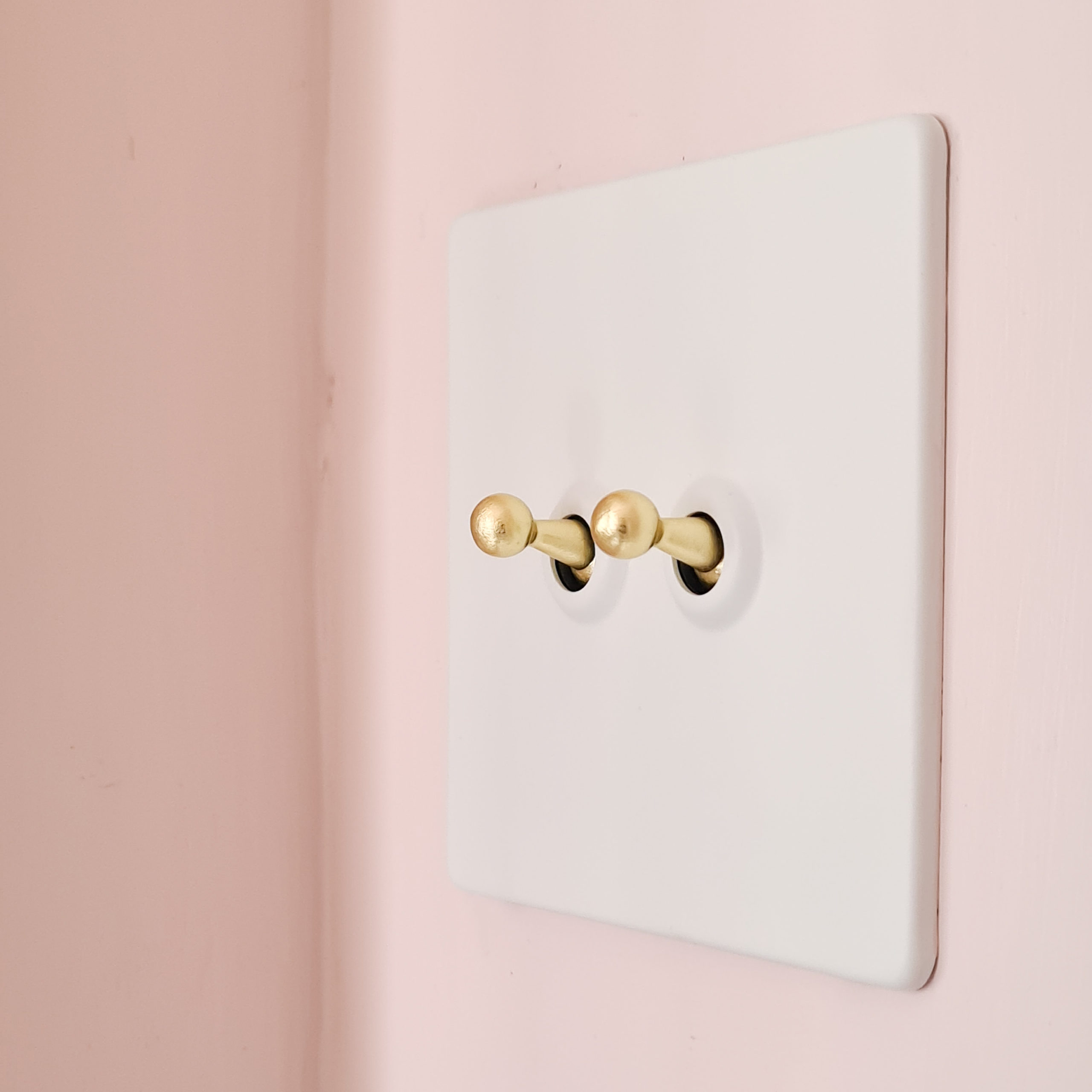 white and gold double toggle switch on soft pink wall