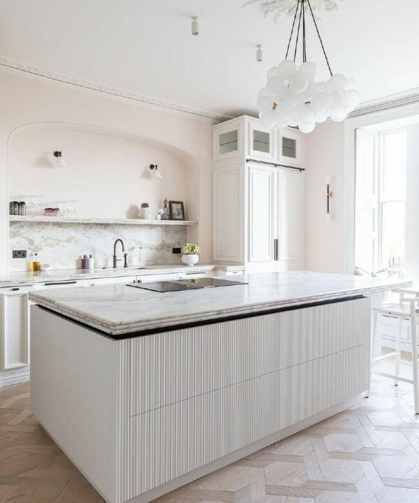 large frosted bubble chandelier suspended above a white marble kitchen island in a soft pink and white kitchen