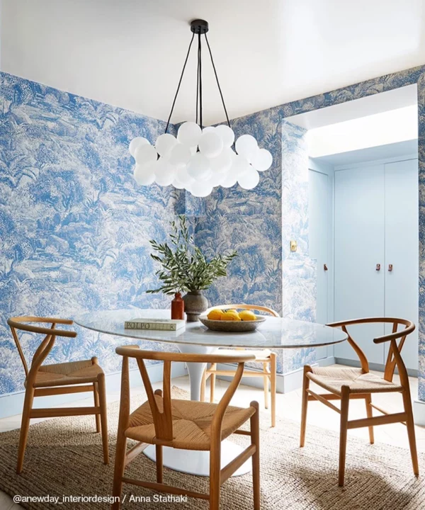 A large frosted bubble chandelier suspended over a round dining table with blue and white wallpaper in the background.